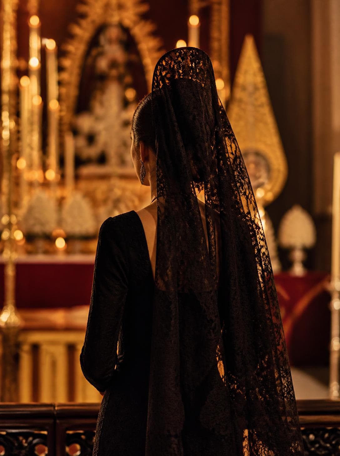Mujer de mantilla sujeta con peineta, de espaldas ante el altar